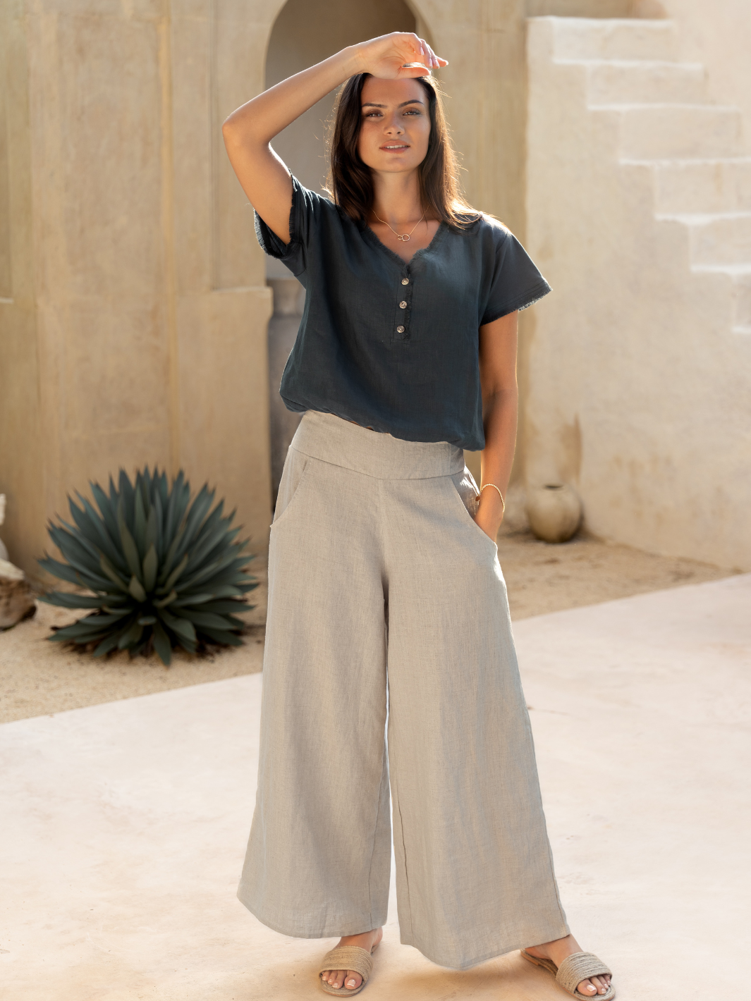 A woman standing in a casual pose wearing flax linen wide-leg pants and a dark top with short sleeves.