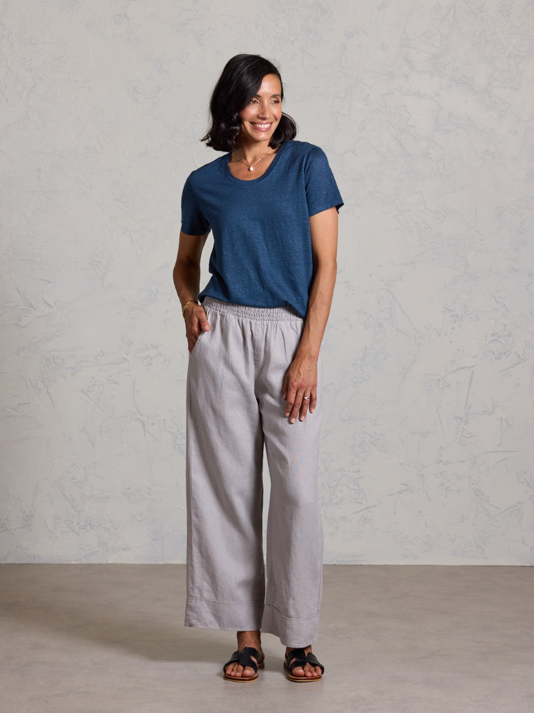 Woman wearing a blue shirt and gray pants against a plain background
