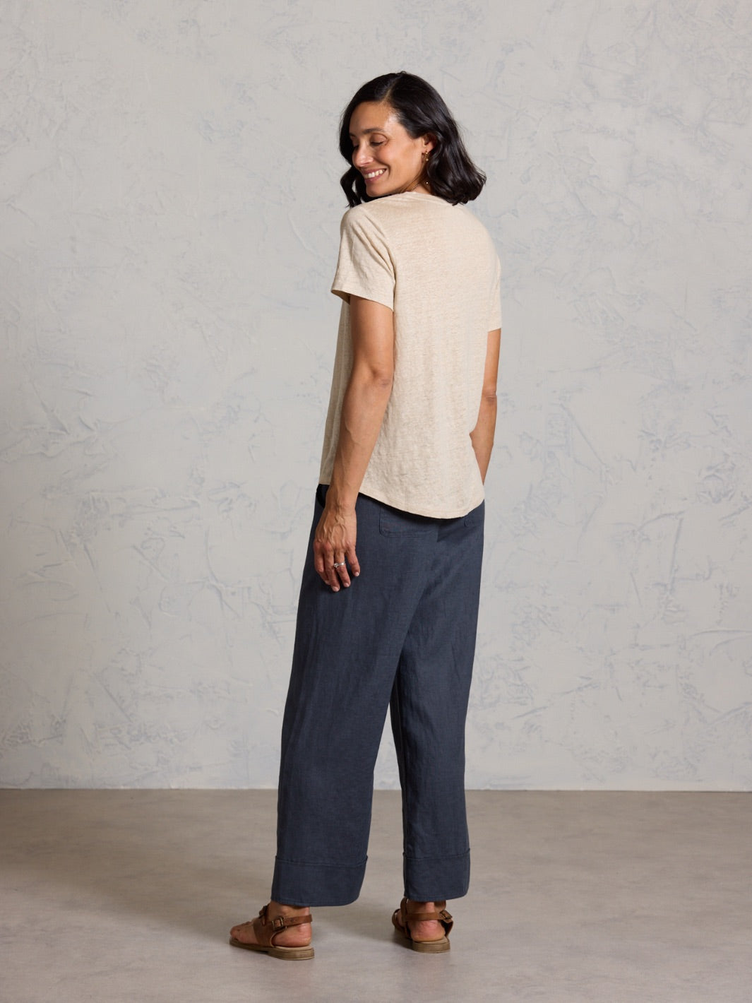 Woman wearing a beige shirt and black pants against a plain background