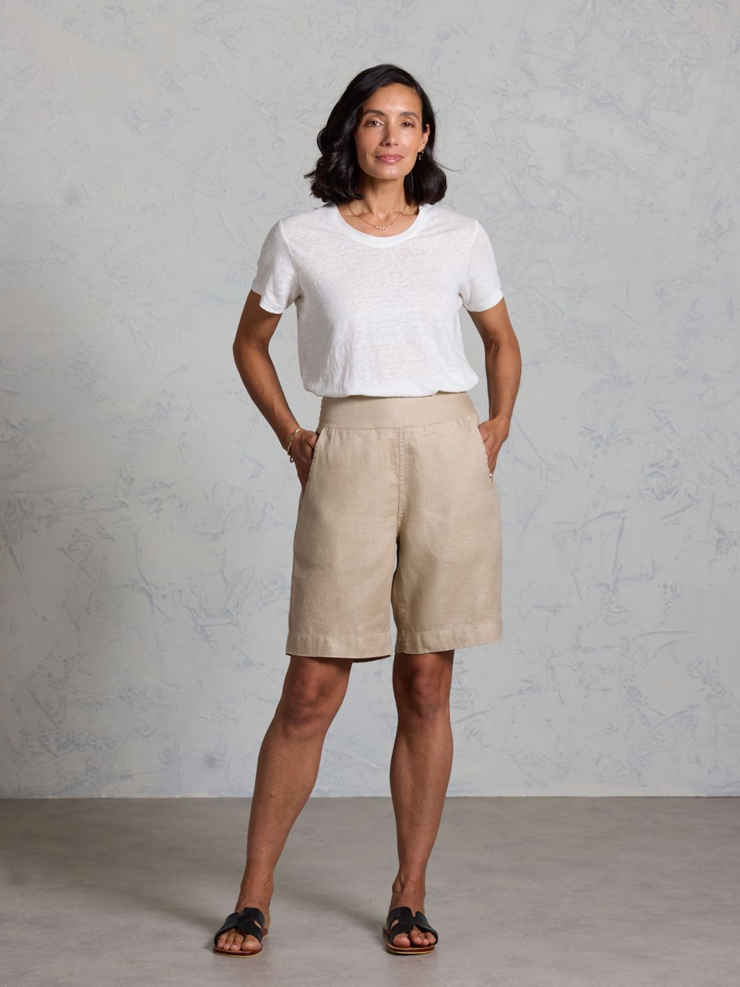 Woman wearing a white t-shirt and beige shorts against a gray background