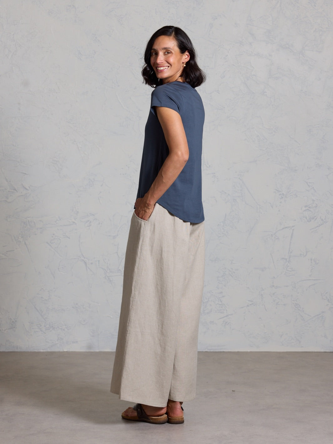 Woman wearing a black top and beige pants against a plain background
