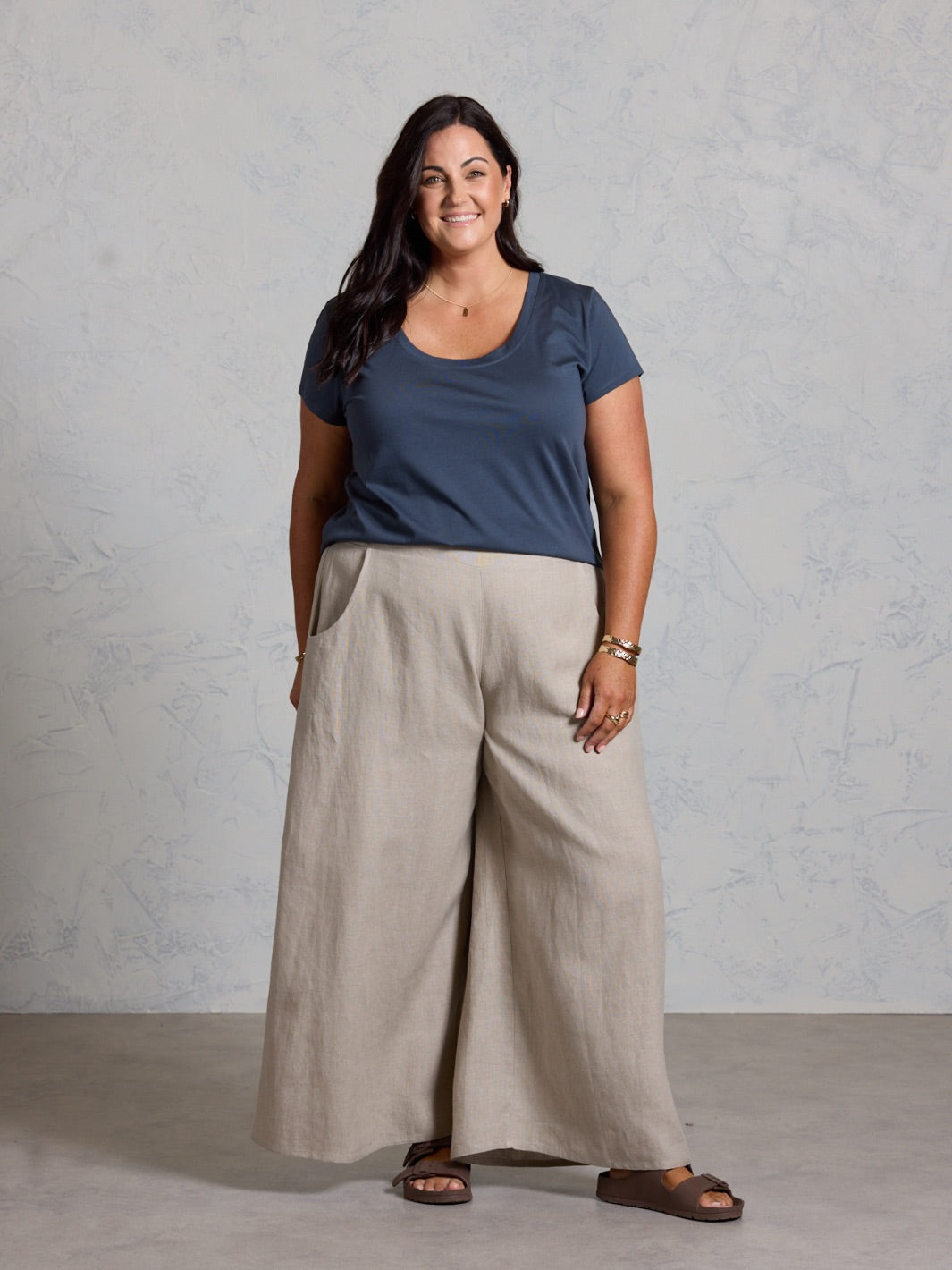 Woman wearing a black shirt and beige pants against a gray background