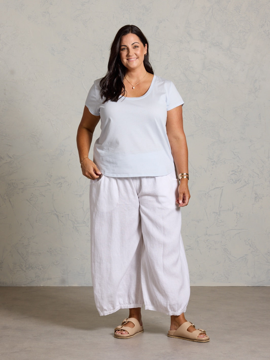Woman wearing a white t-shirt and light-colored pants against a neutral background