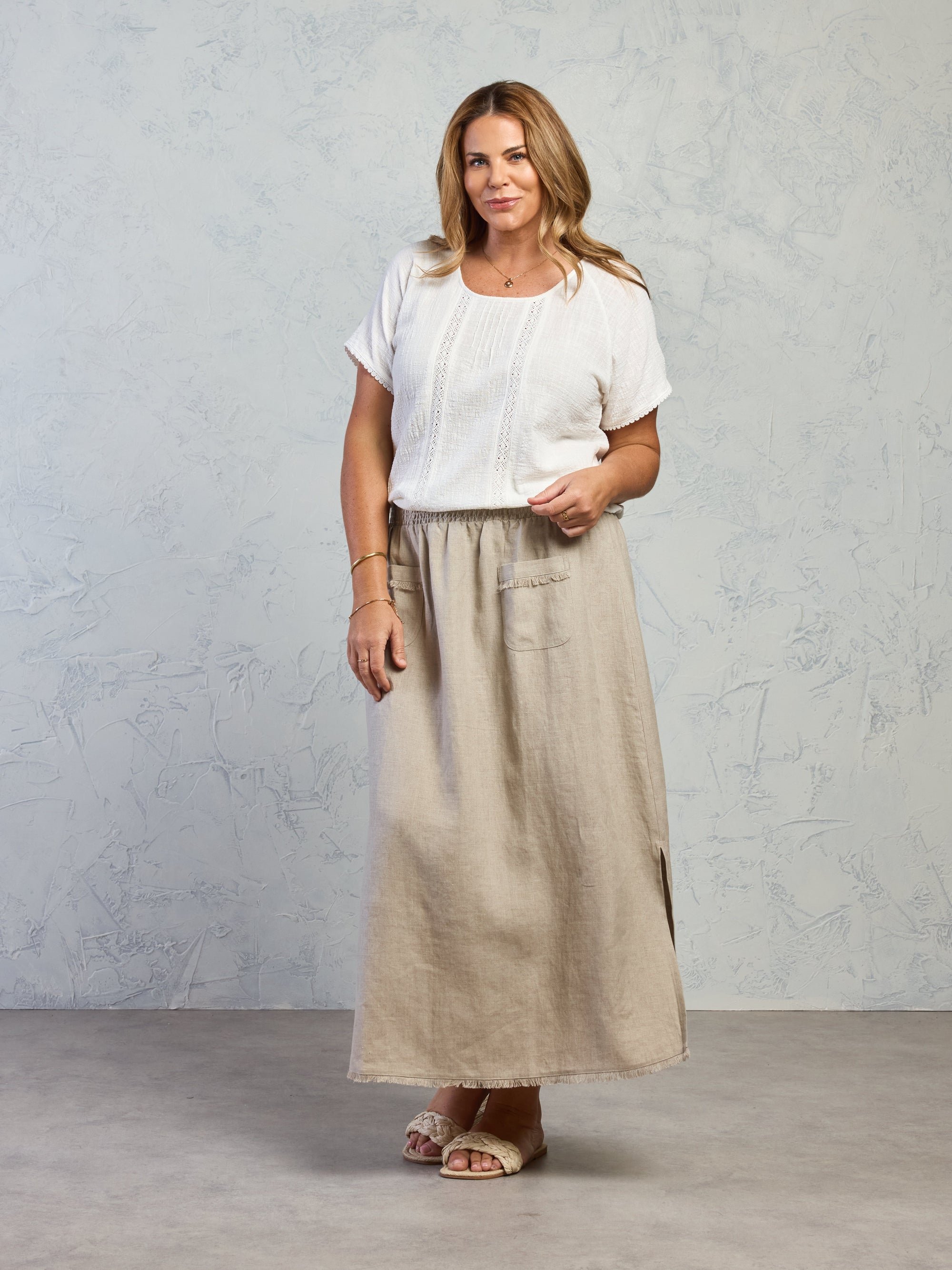 Woman wearing a white top and beige skirt against a gray background