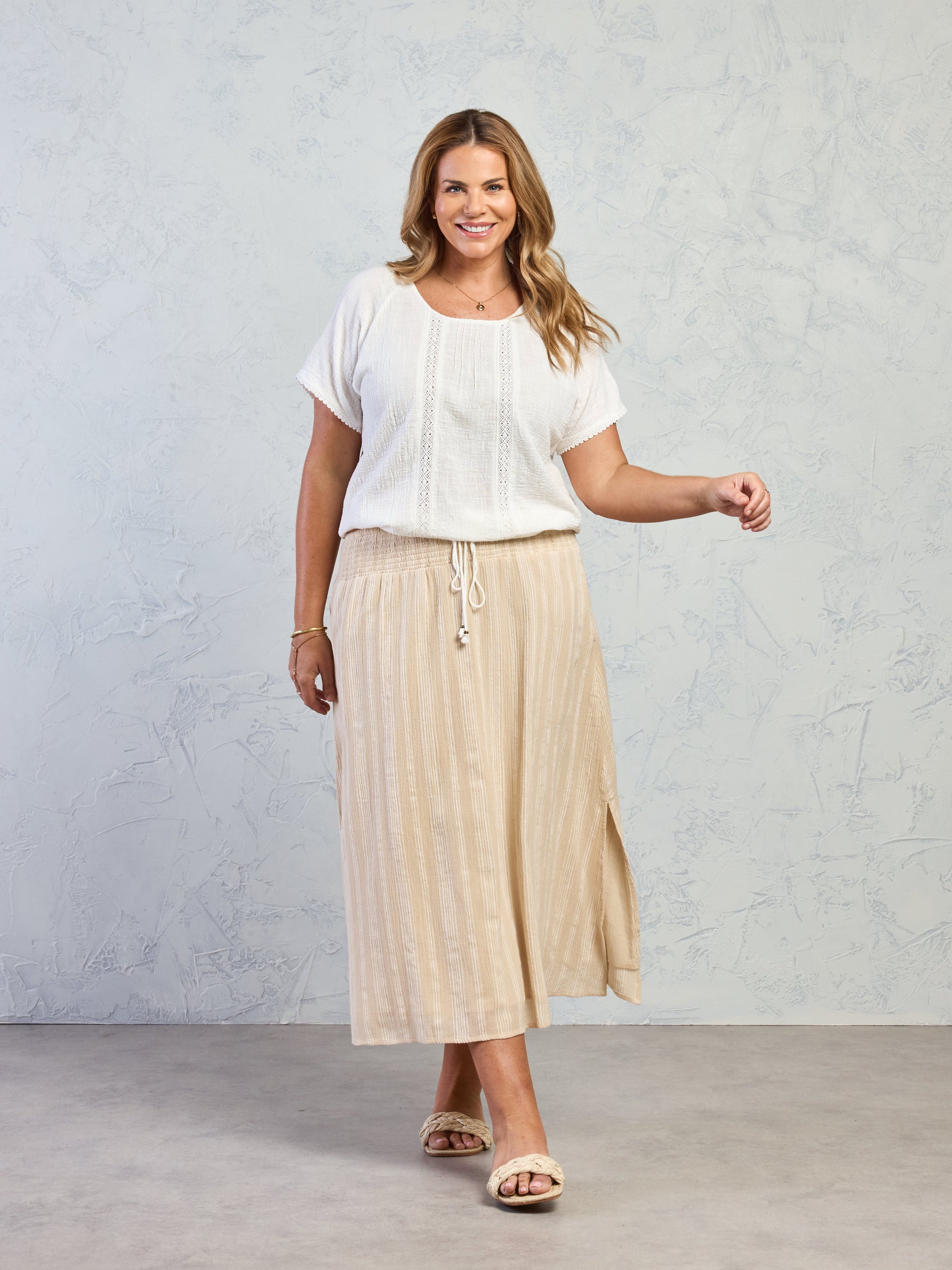 Woman wearing a white top and beige skirt against a plain background