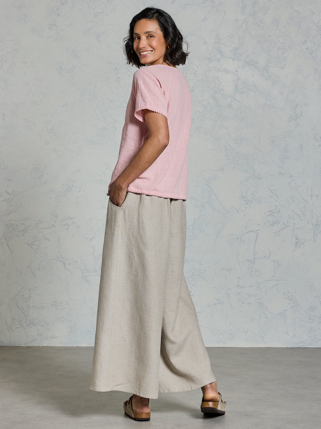 Woman wearing a pink top and beige pants against a plain background