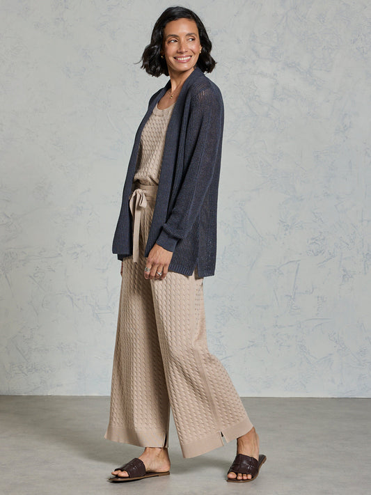 Woman wearing a navy cardigan and beige pants against a gray background