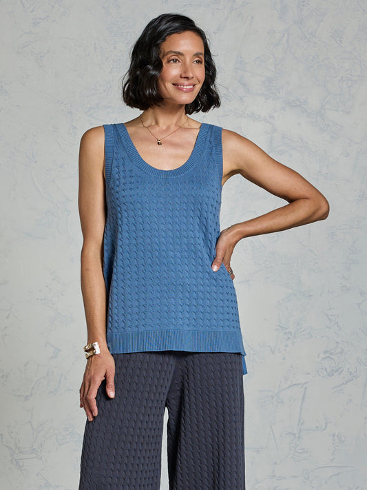 Woman wearing a blue sleeveless top and dark pants against a gray background