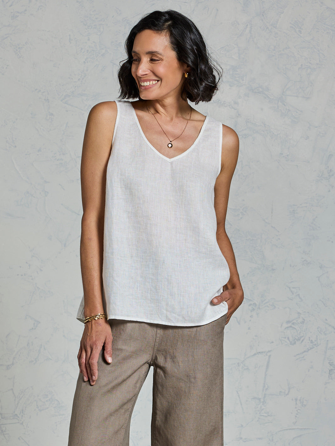 Woman wearing a white sleeveless top and brown pants against a gray background