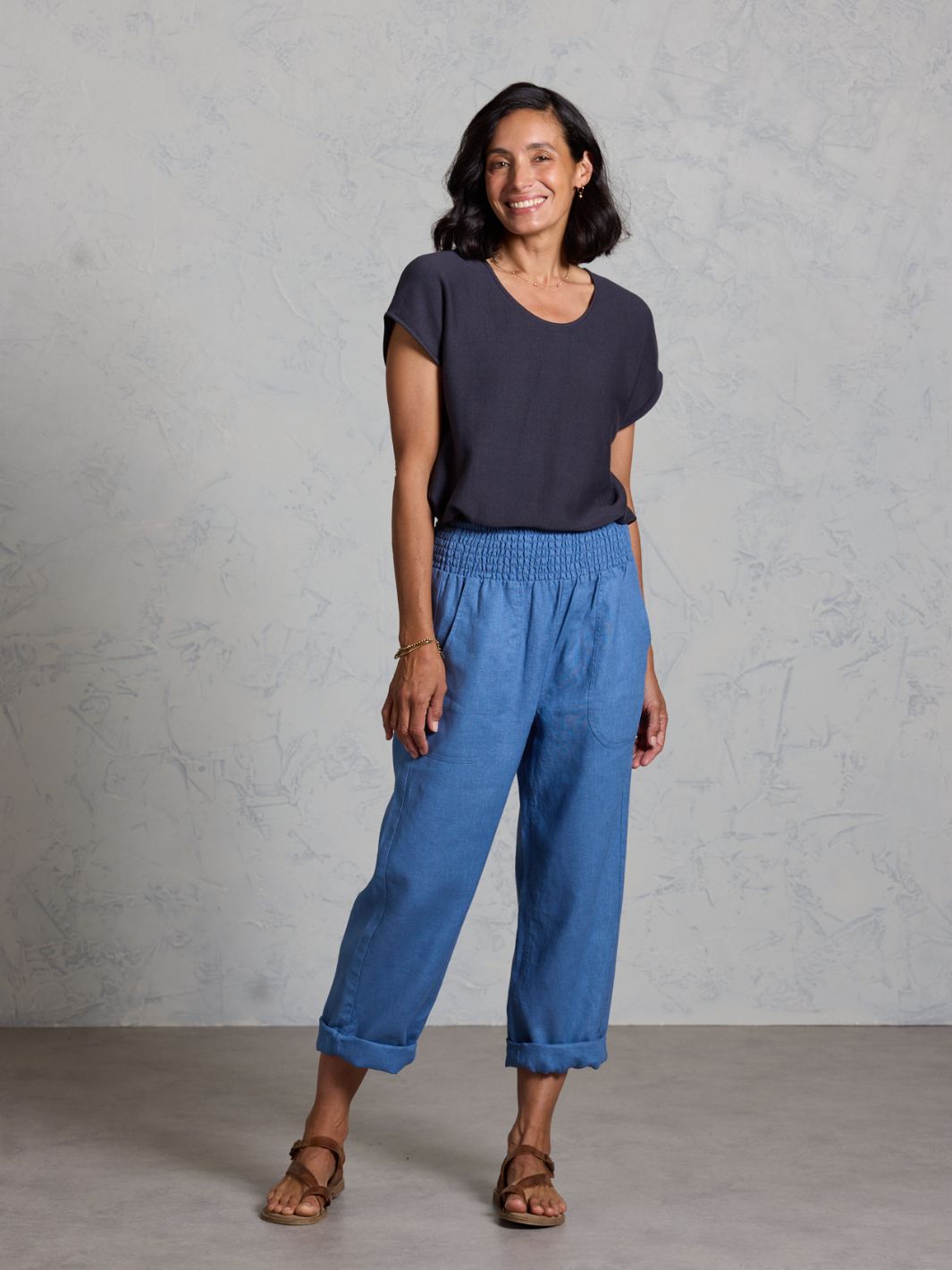 Woman wearing a dark blue top and blue pants against a gray background