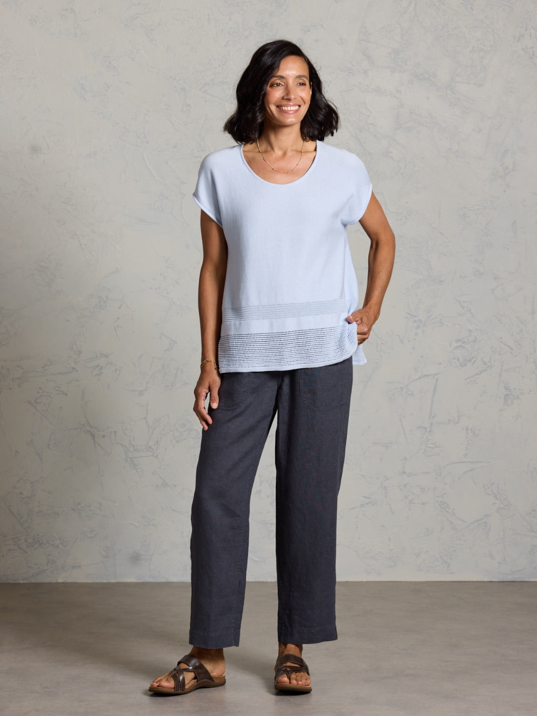 Woman wearing a light blue top and dark pants against a plain background