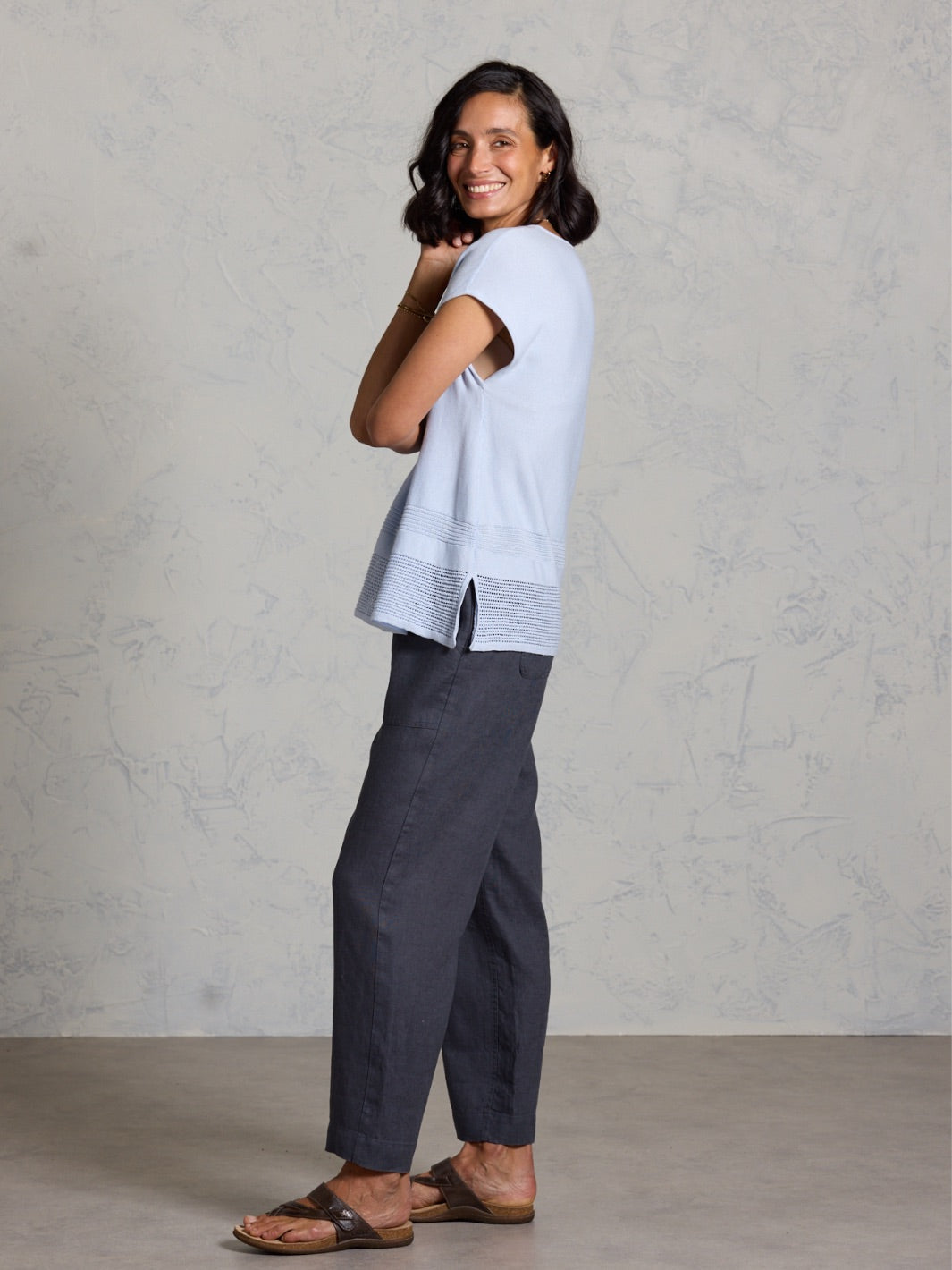 Woman wearing a light blue top and dark pants against a plain background