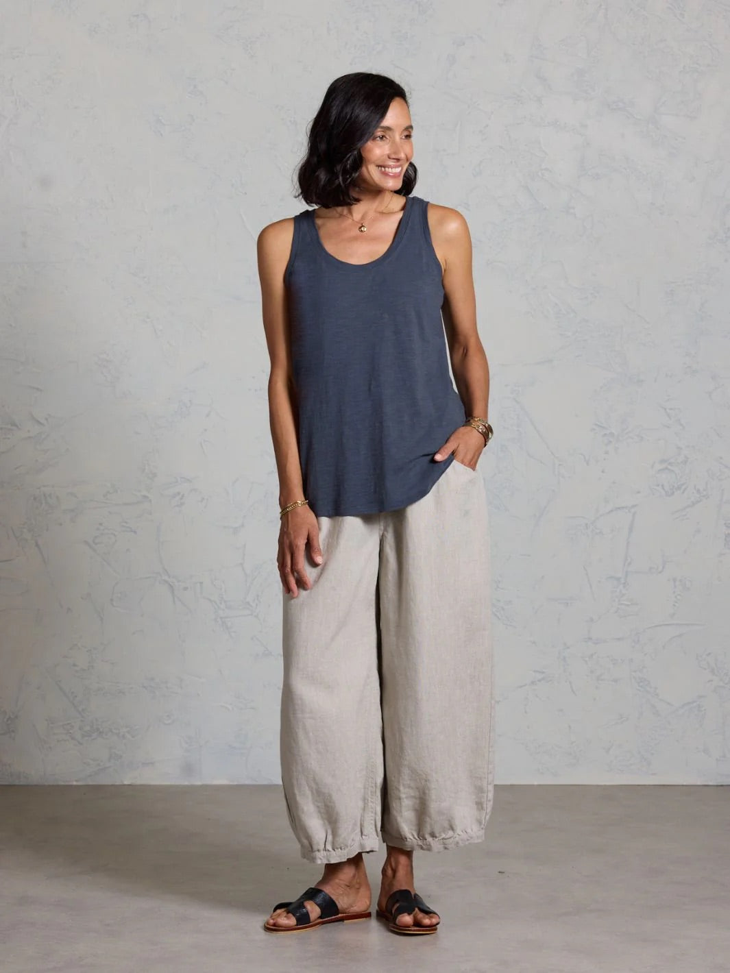 Woman wearing a dark tank top and light gray wide-leg pants against a plain background