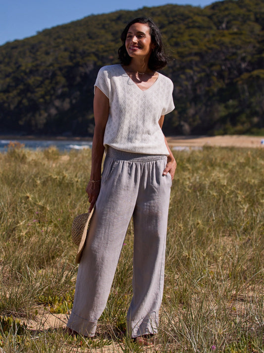 Woman standing in a natural setting wearing a light top and gray pants.