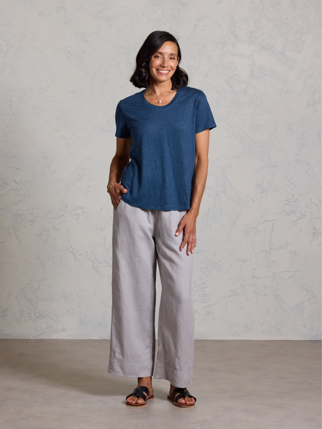 Woman wearing a blue t-shirt and light gray pants against a plain background