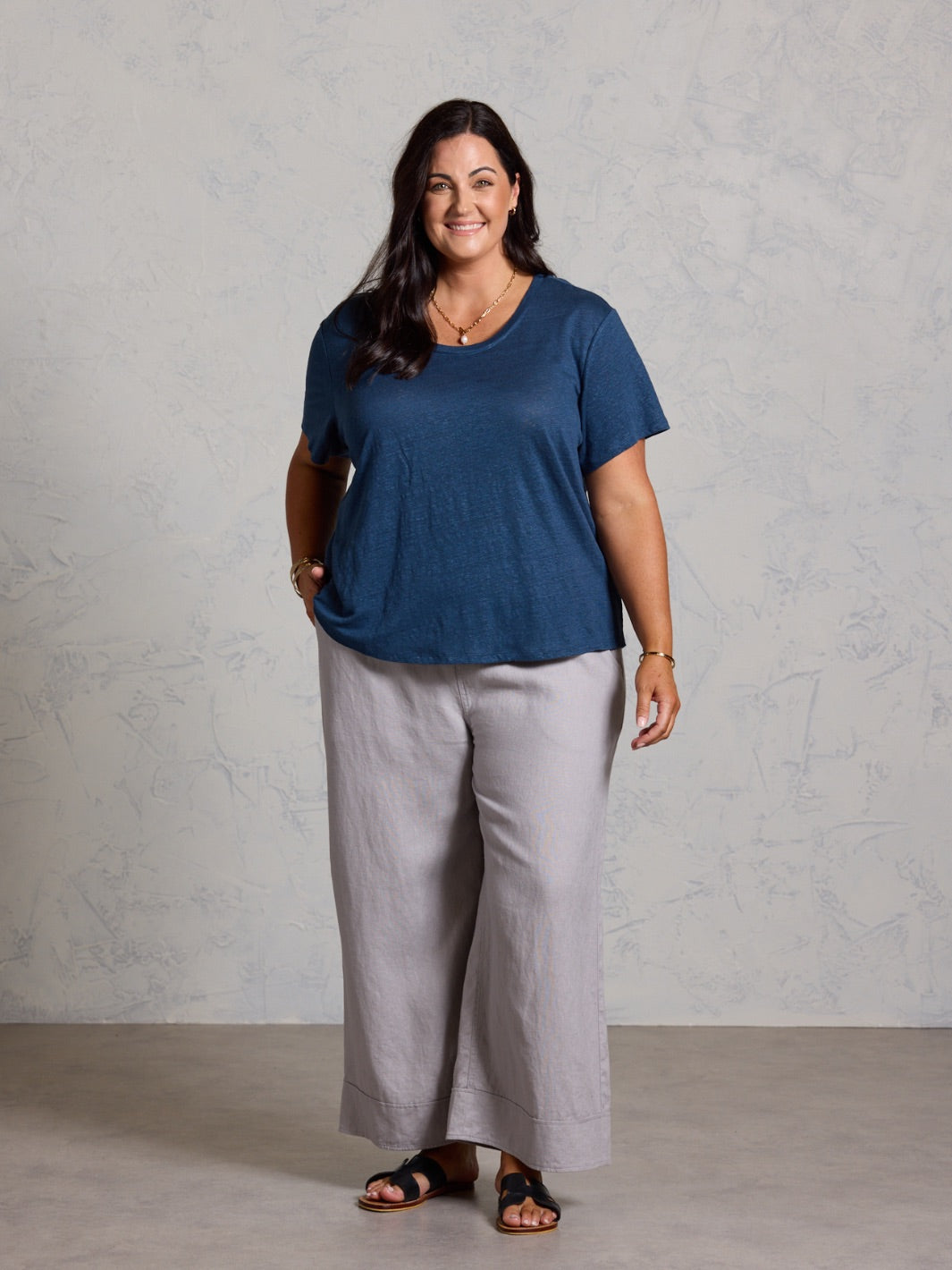 Woman wearing a blue shirt and gray pants against a plain background