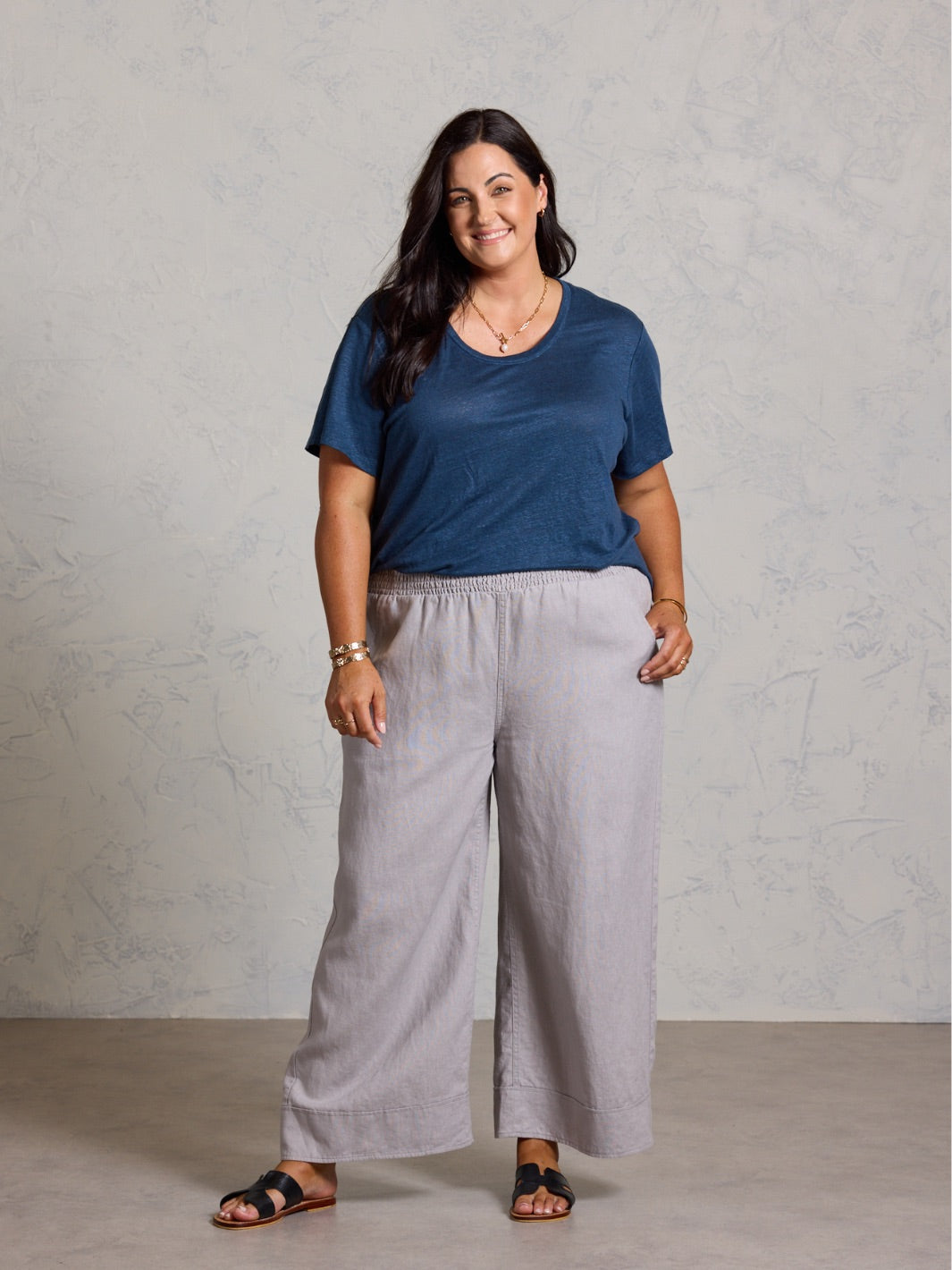 Woman wearing a blue top and gray pants against a plain background