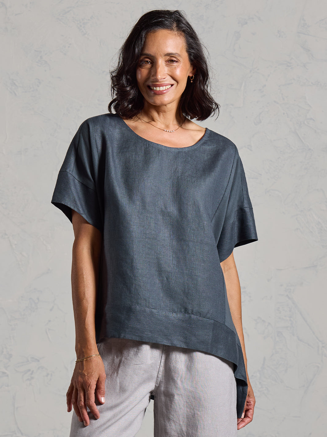Woman wearing a dark top and light gray pants against a gray background