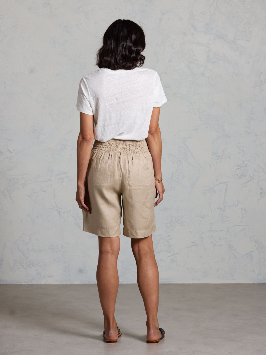 Person wearing beige shorts and a white shirt against a plain background