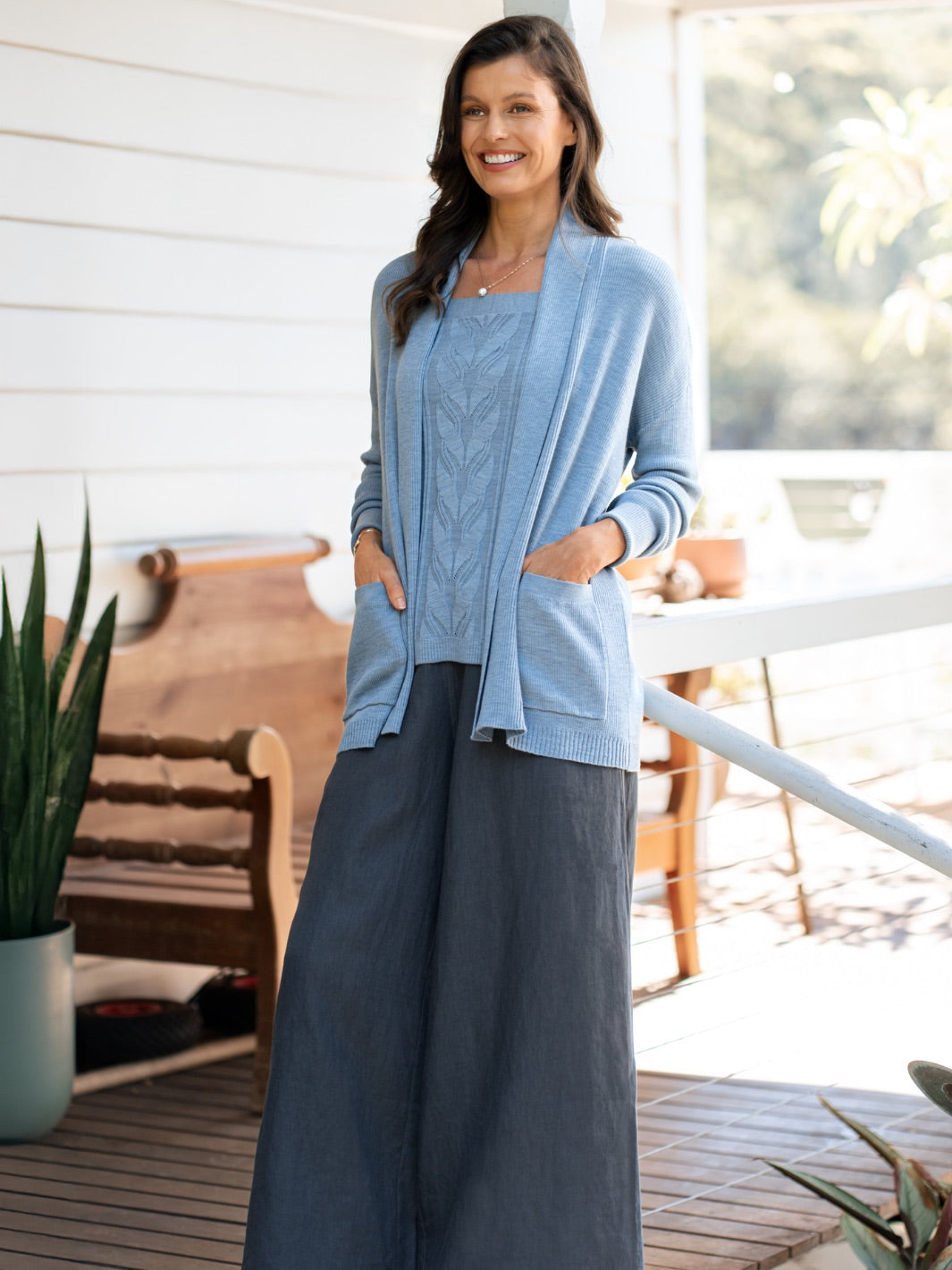 Woman wearing a light blue cardigan over a dark top on a wooden deck.
