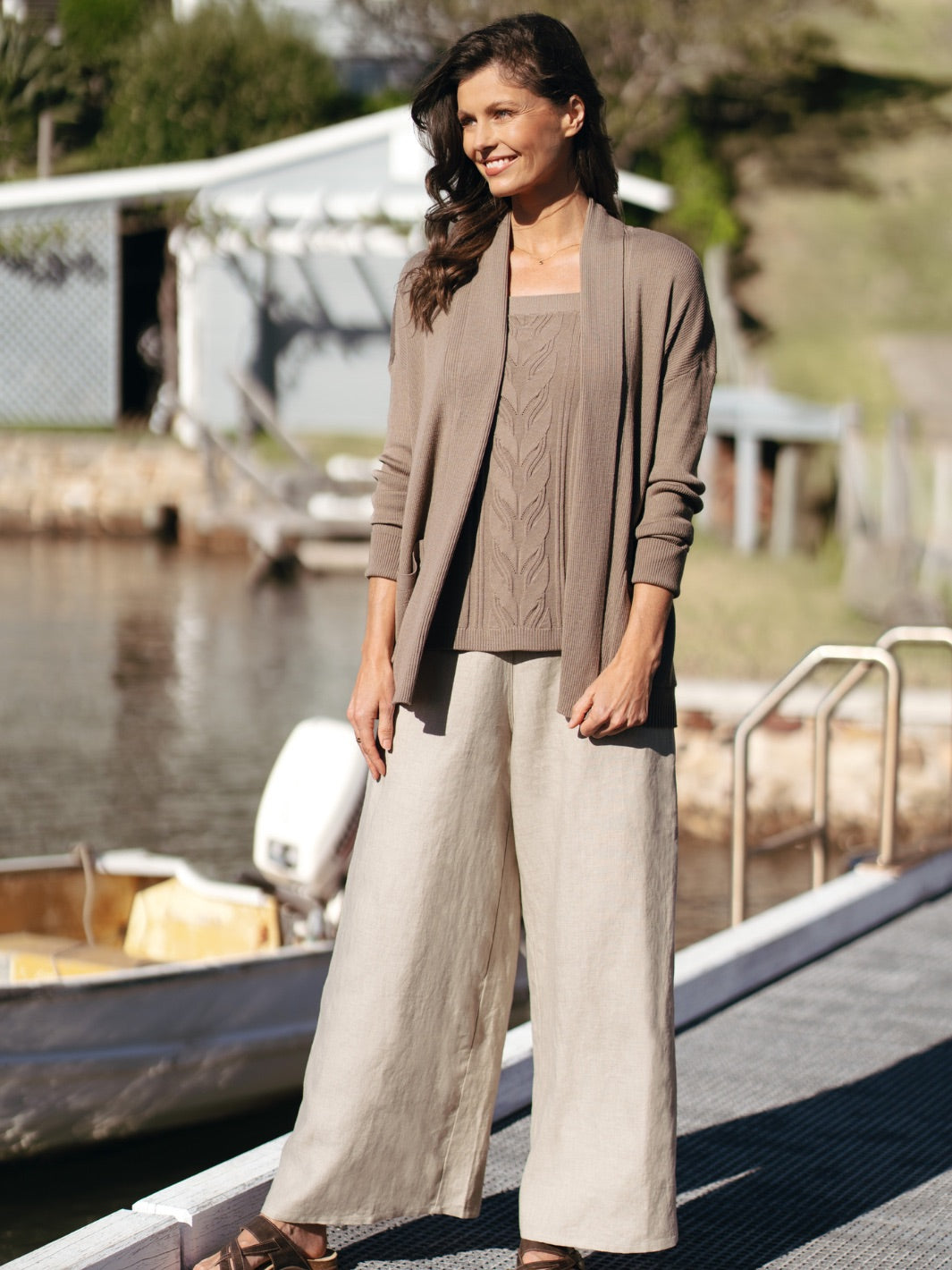 Woman in a brown cardigan and beige pants standing by a waterfront.