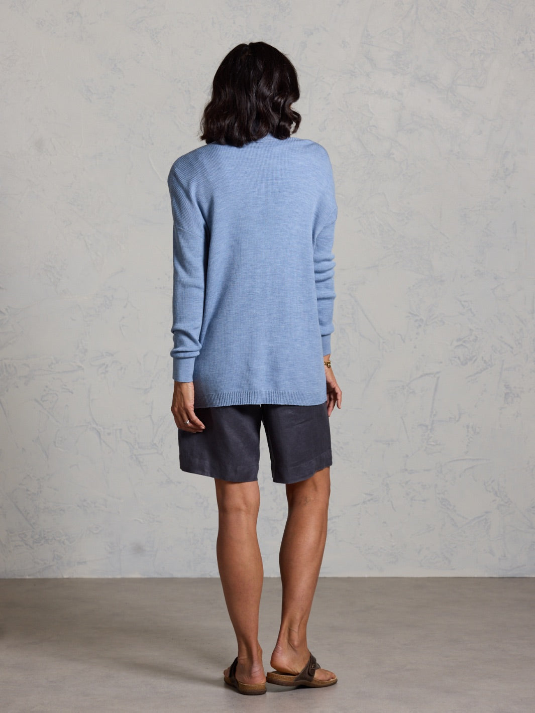 Person wearing a blue sweater and dark shorts against a gray background