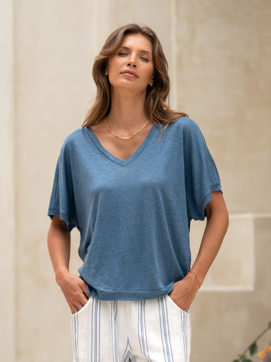 Woman wearing a blue top and white pants with black stripes against a neutral background