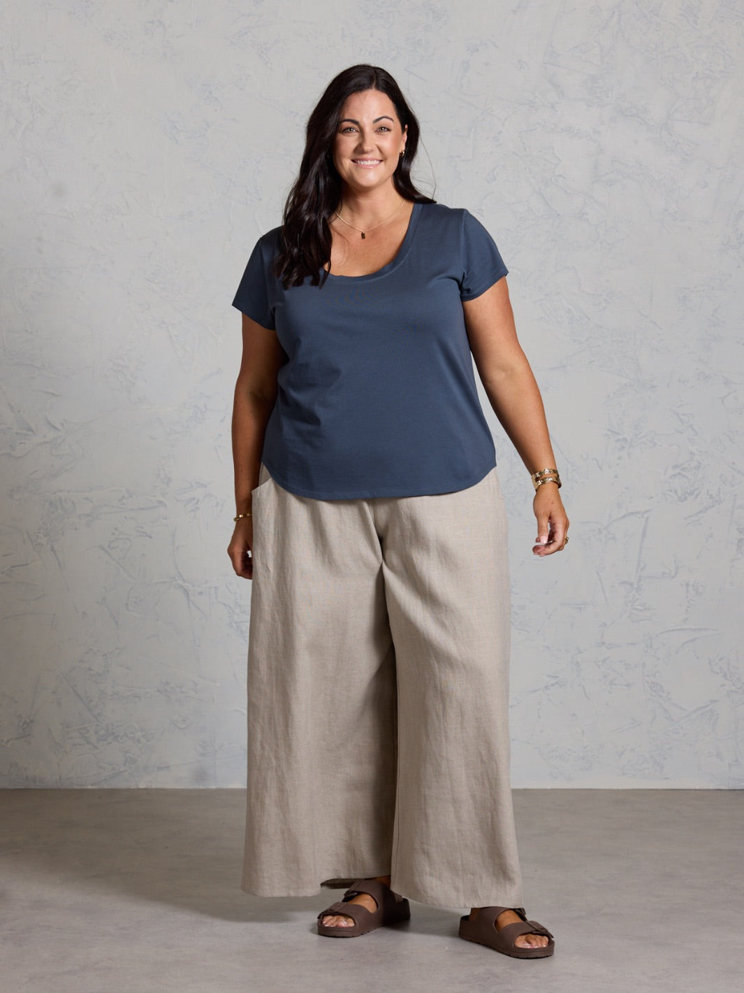 Woman wearing a black shirt and beige pants against a plain background