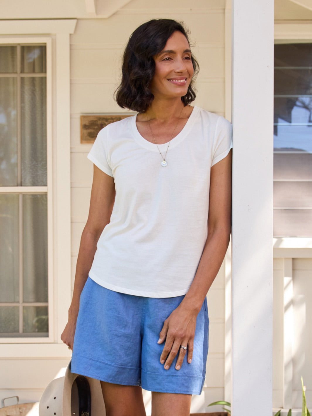 Woman wearing a white t-shirt and blue shorts standing on a porch.