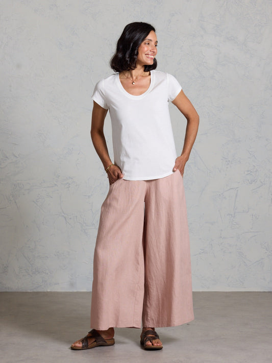 Woman wearing a white t-shirt and pink wide-leg pants against a gray background