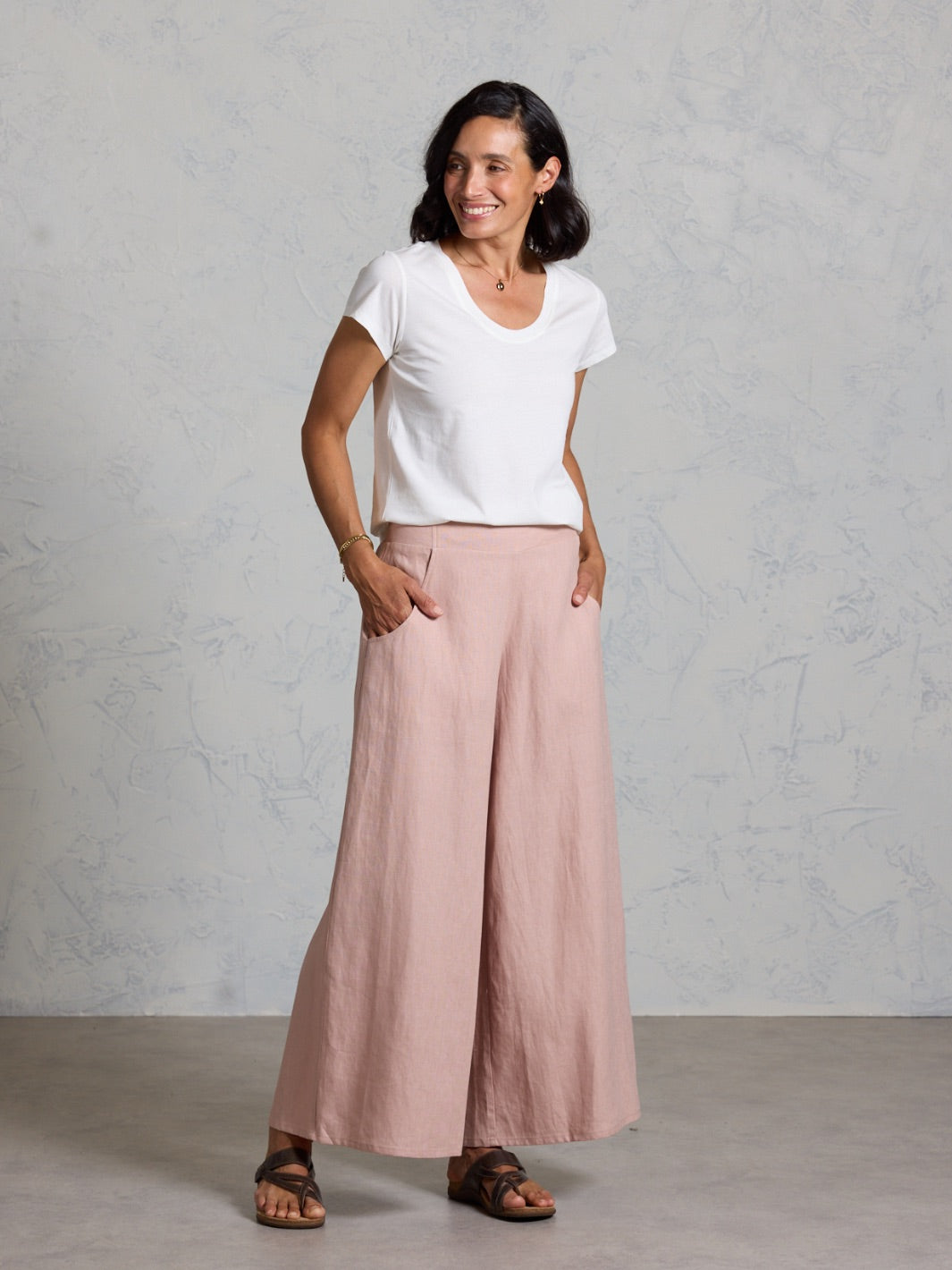 Woman wearing a white t-shirt and pink wide-leg pants against a gray background