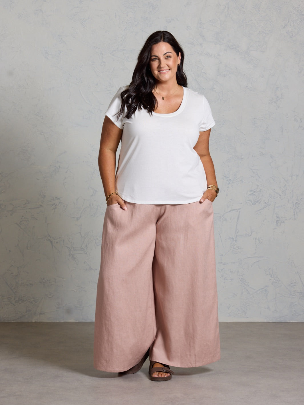 Woman wearing a white t-shirt and pink wide-leg pants against a gray background