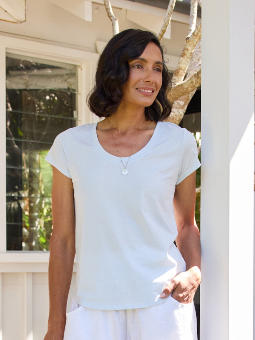 Woman wearing a light blue t-shirt and white pants standing outdoors.