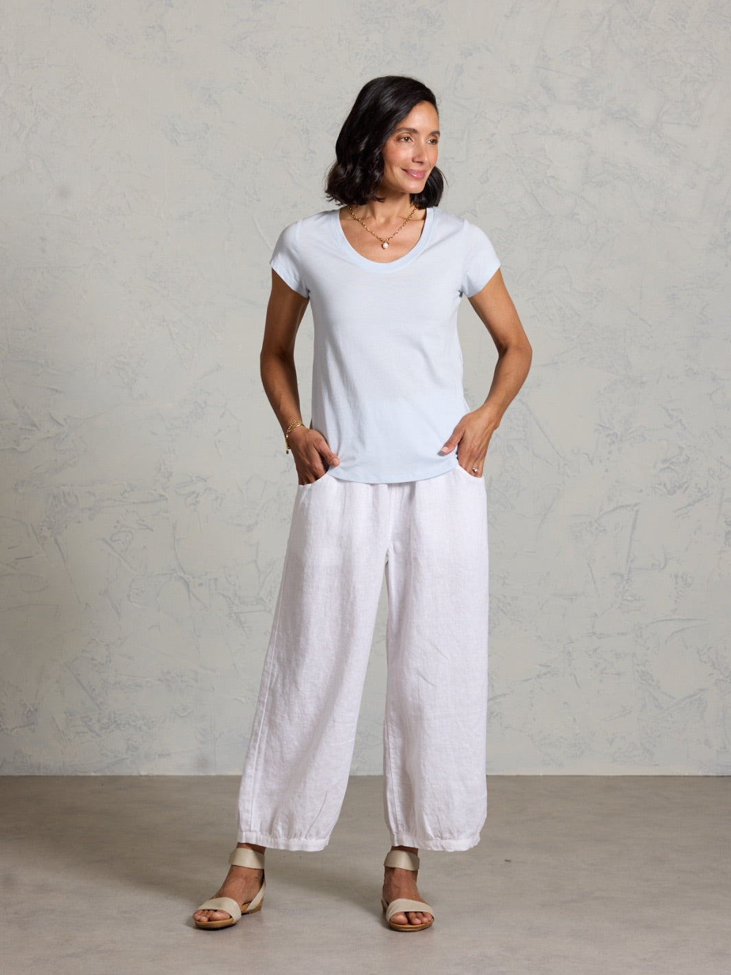 Woman wearing a white t-shirt and light-colored pants against a plain background