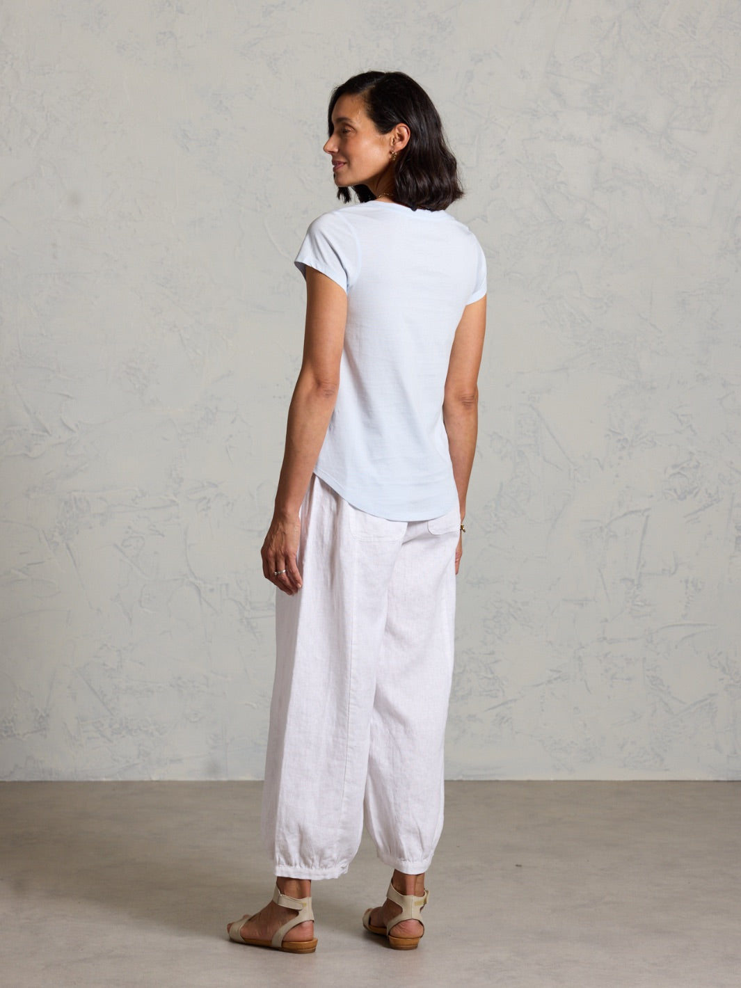 Person wearing a white t-shirt and light-colored pants against a plain background