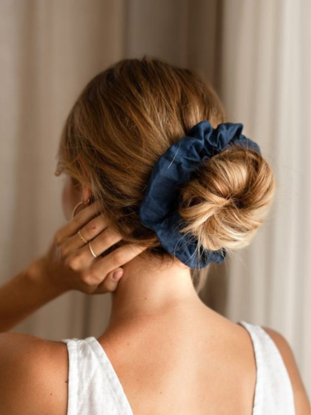 Woman with a styled hair bun featuring a blue scrunchie against a neutral background