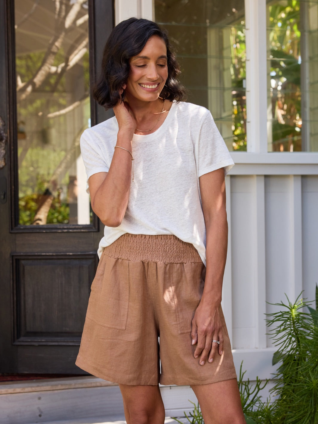 Woman wearing a white top and brown shorts standing on a porch.