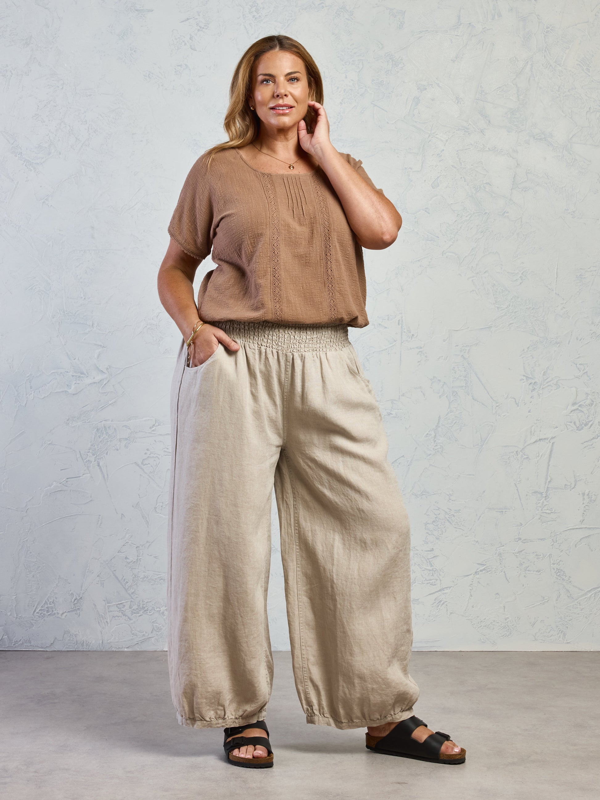 Woman wearing a brown top and beige wide-leg pants against a light gray background