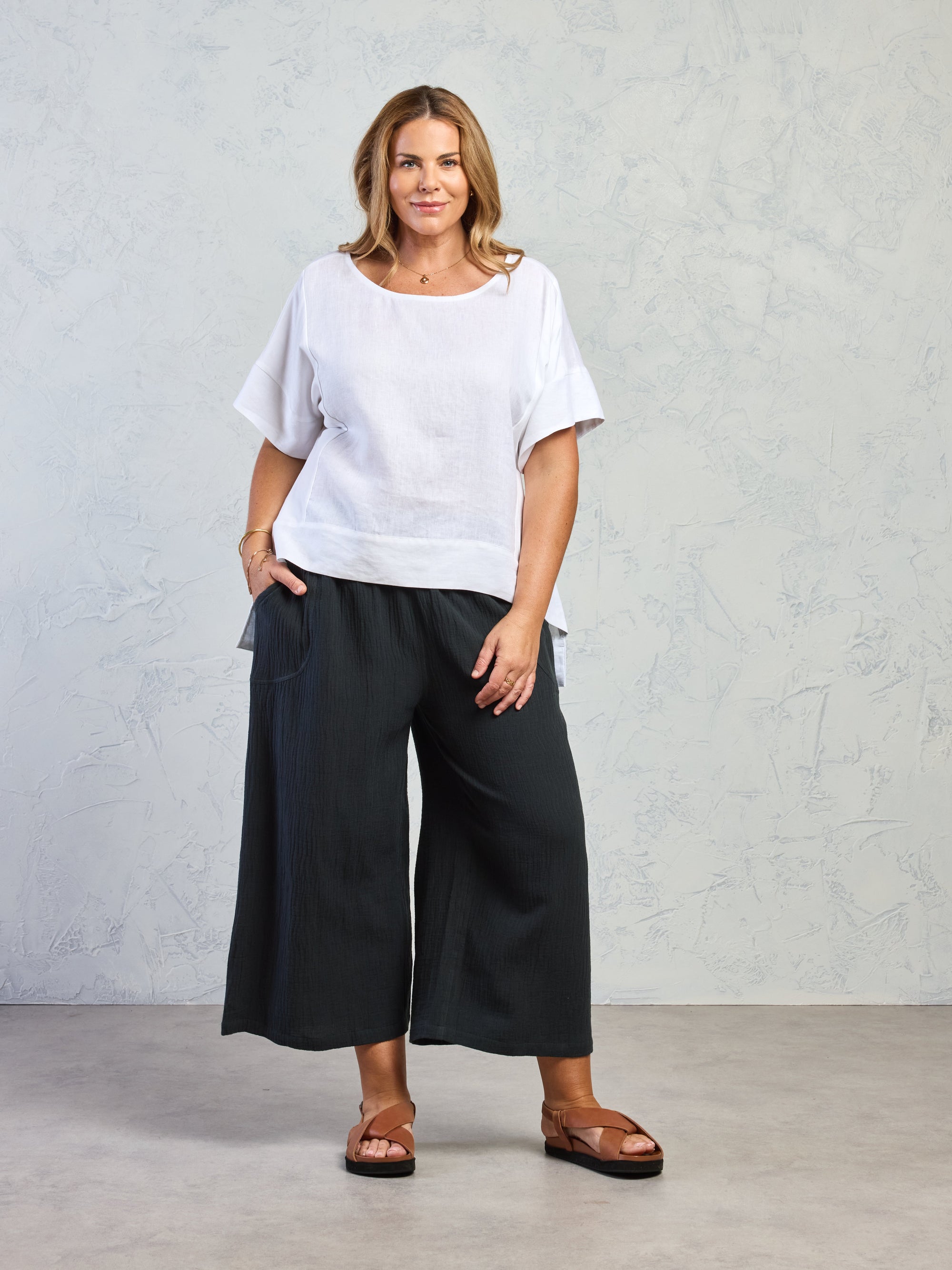 Woman wearing a white top and black pants against a plain background