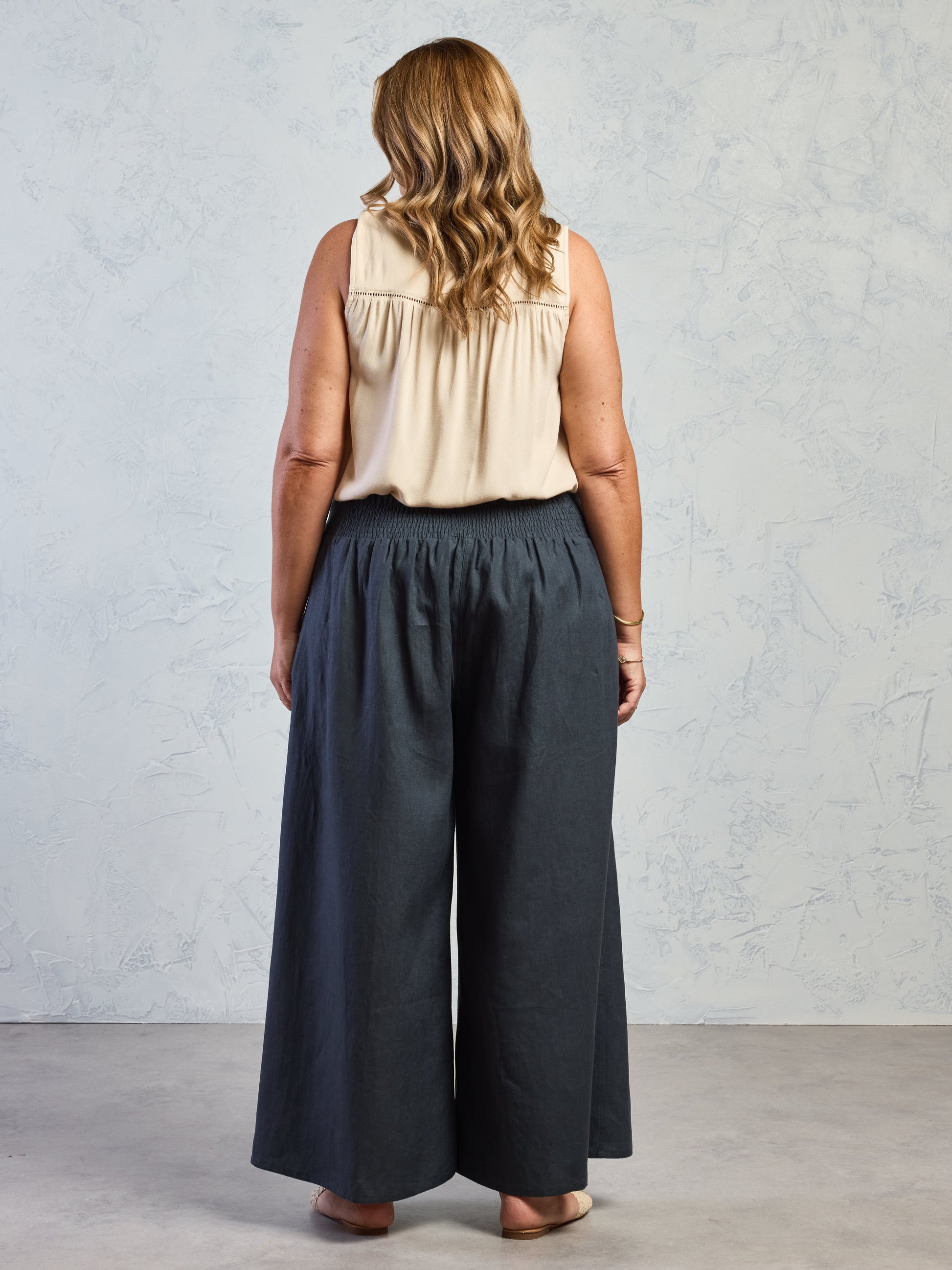 Woman wearing a beige top and dark blue wide-leg pants against a light gray background