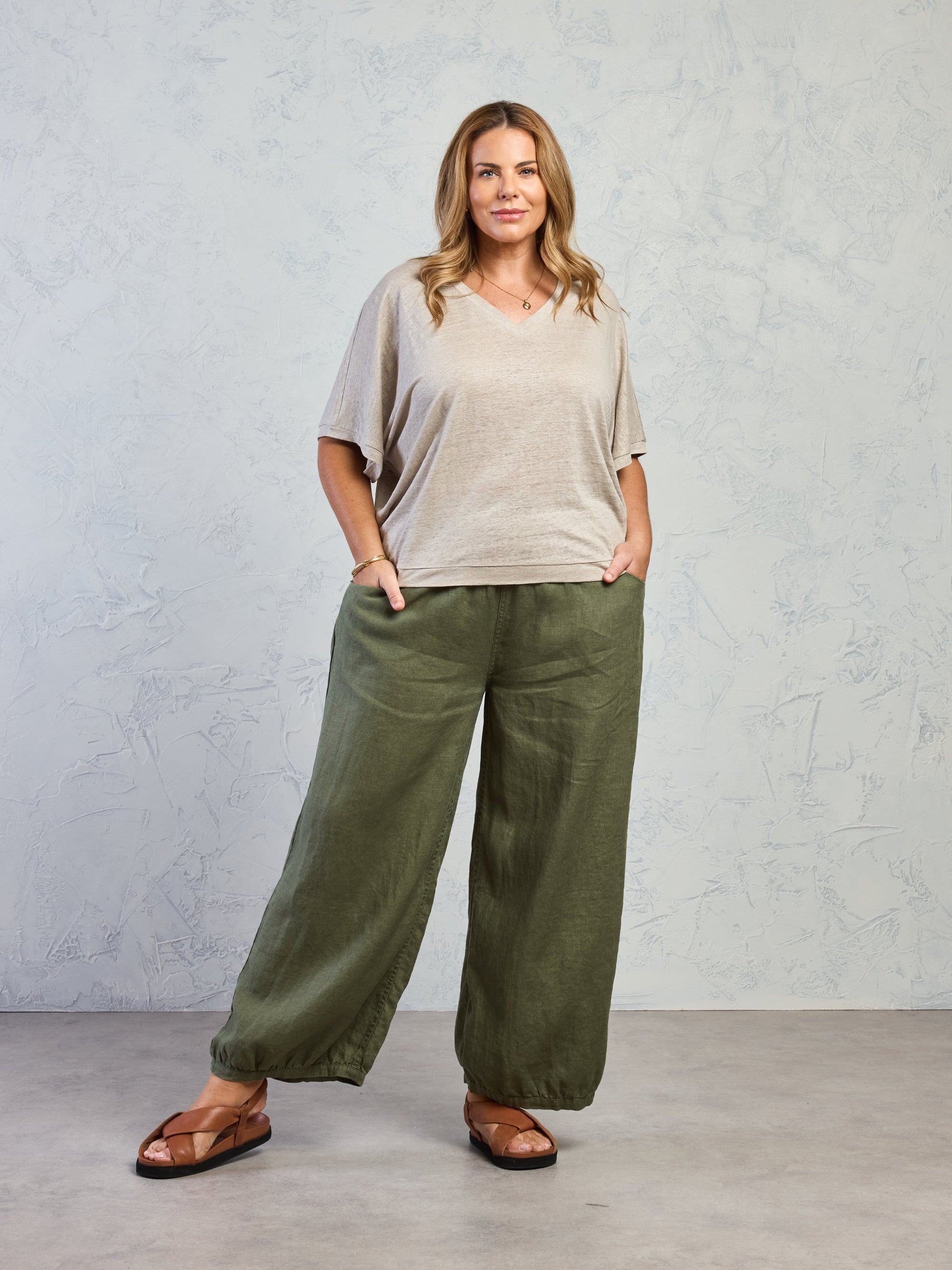 Woman wearing a beige top and green wide-leg pants against a gray background