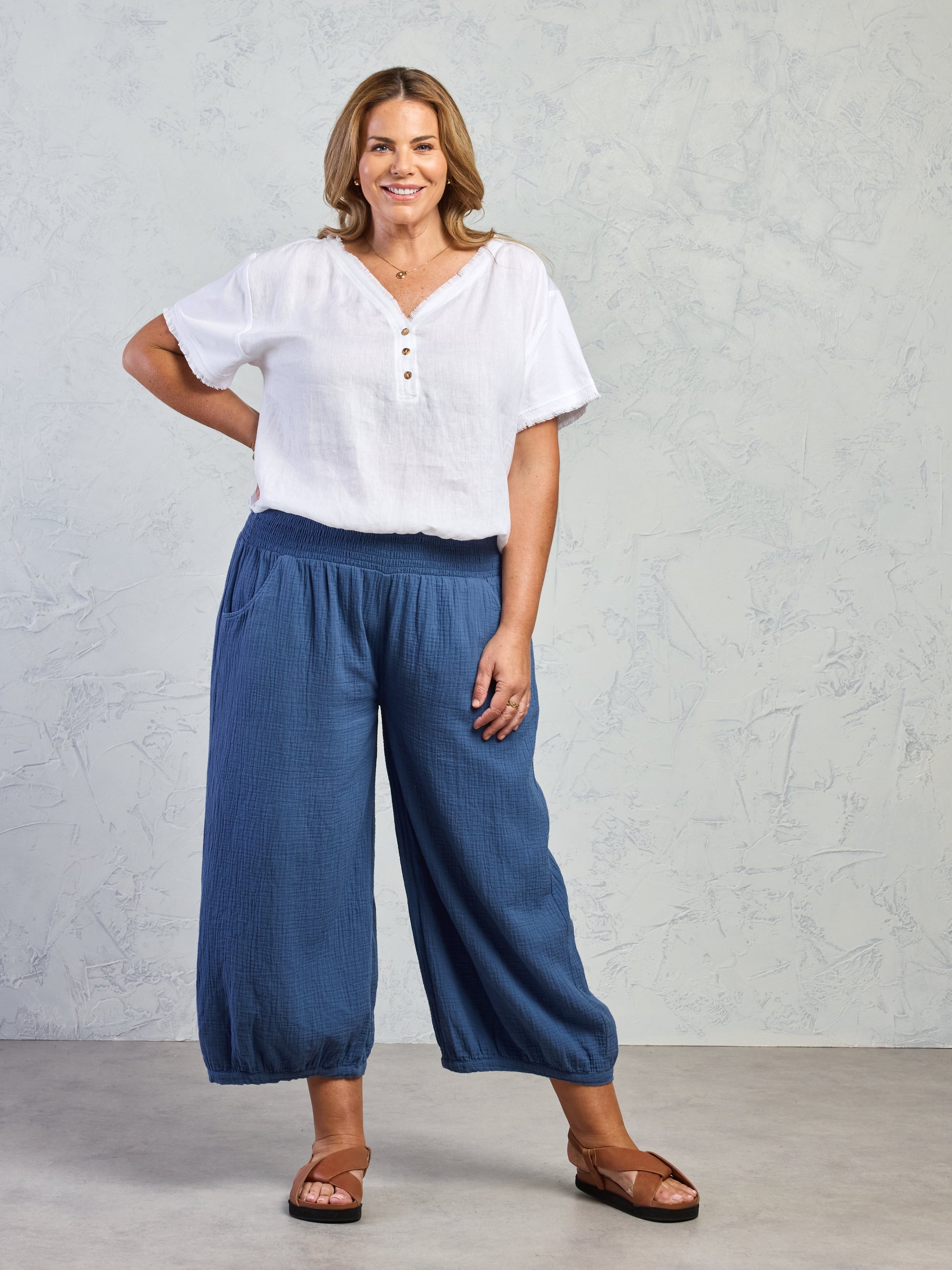Woman wearing a white blouse and blue pants against a plain background