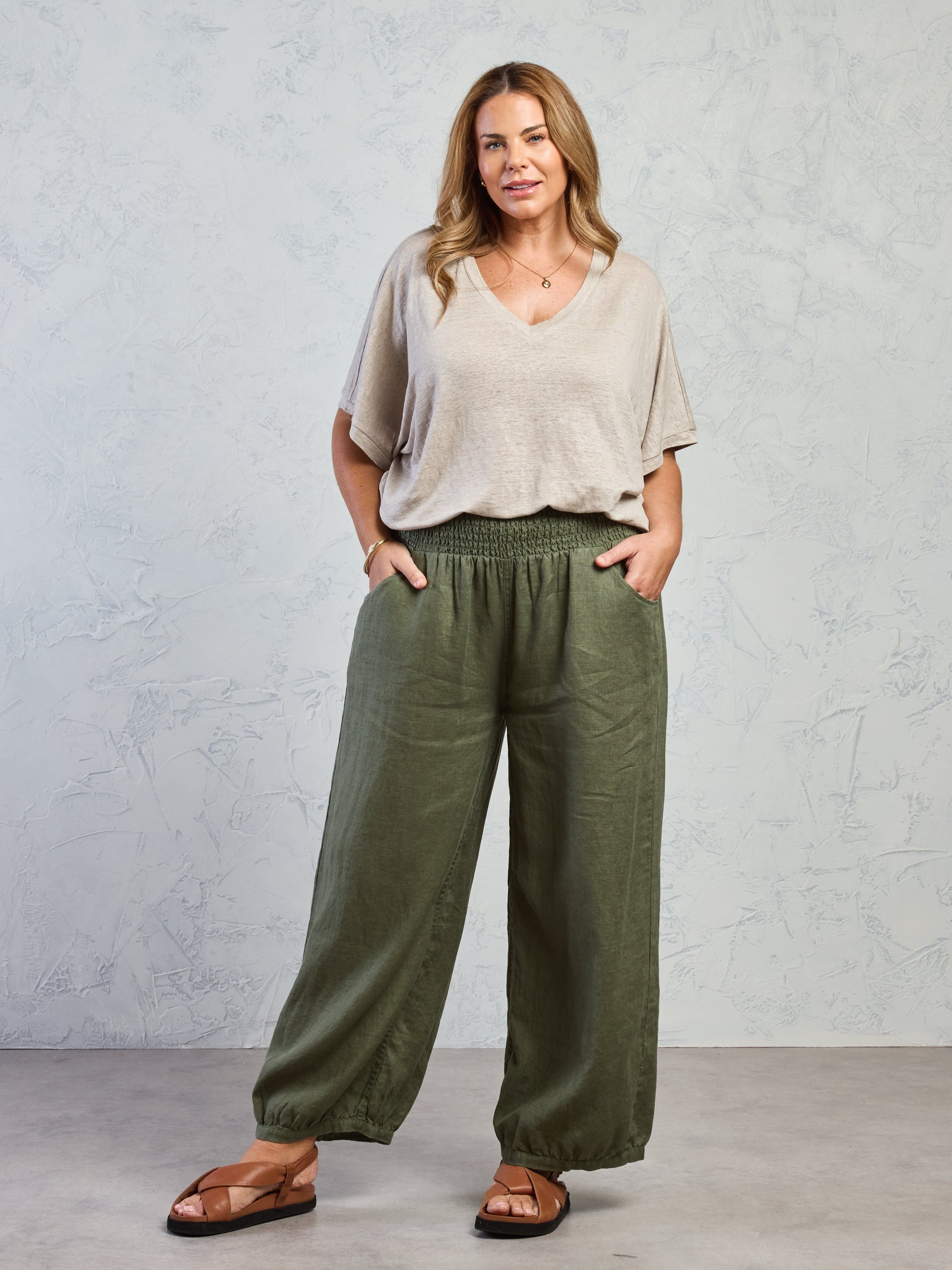 Woman wearing a beige top and green wide-leg pants against a gray background