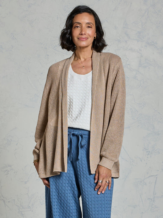 Woman wearing a beige cardigan, white sweater, and blue pants against a gray background