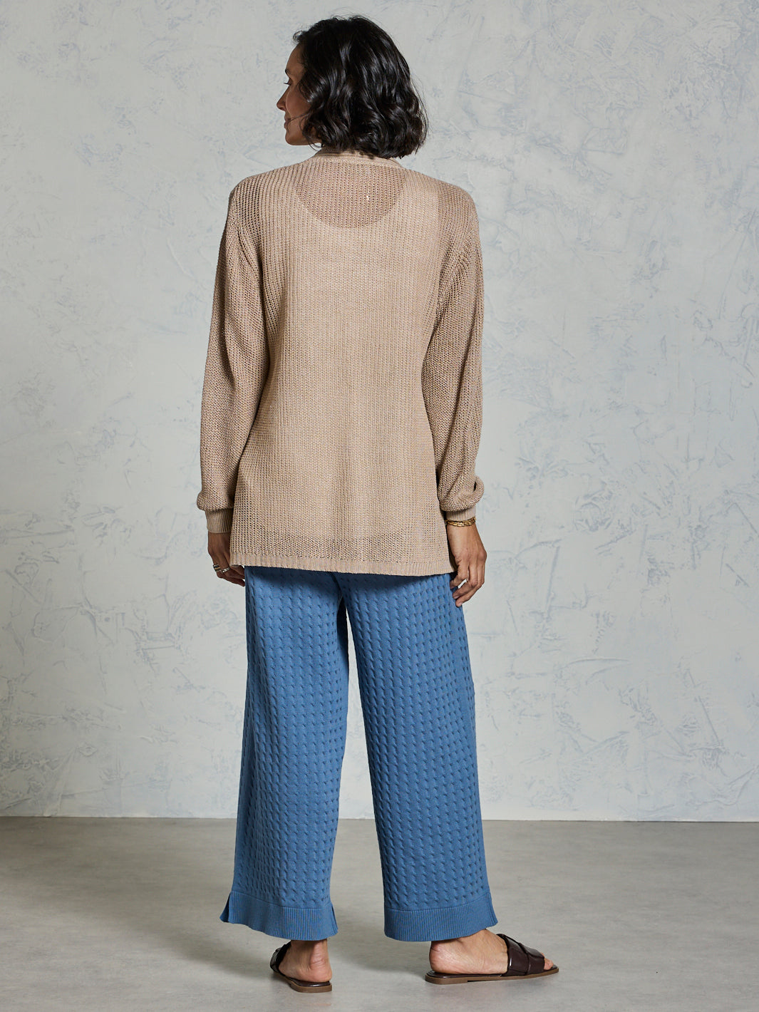 Person wearing a beige sweater and blue pants against a plain background