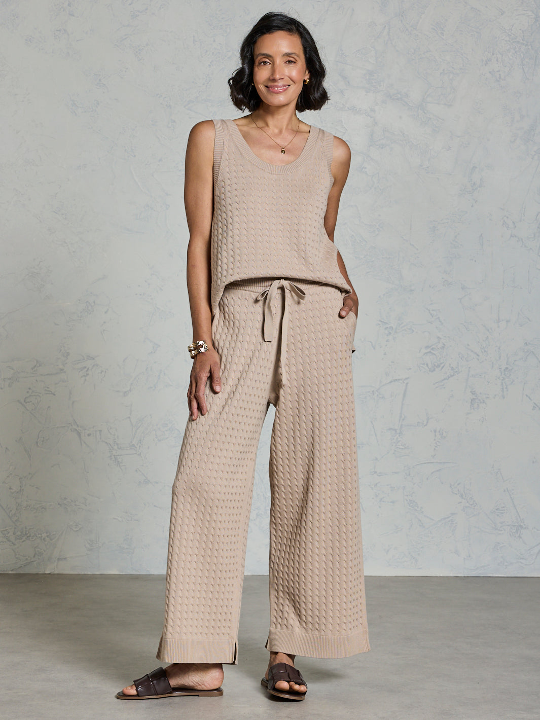 Woman wearing a beige sleeveless top and wide-leg pants against a plain background