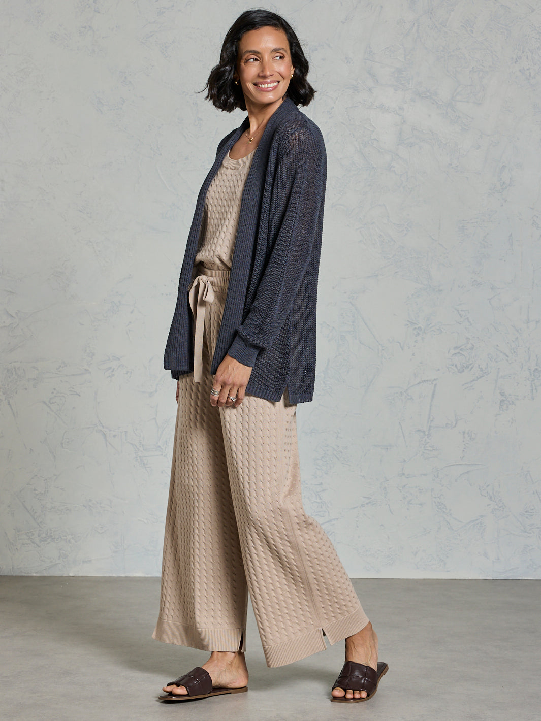 Woman wearing a navy cardigan and beige pants against a gray background