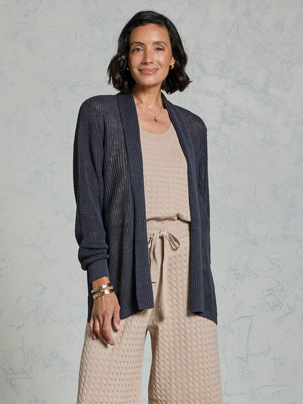 Woman wearing a navy cardigan over a beige top and pants on a gray background