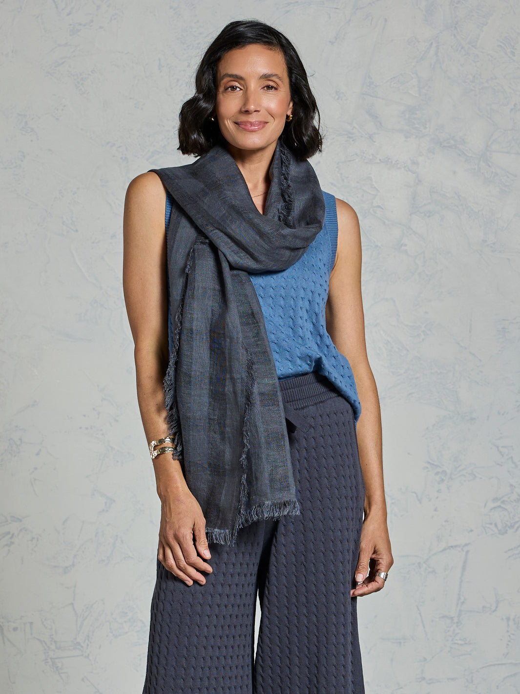 Woman wearing a dark gray scarf and blue top against a gray background