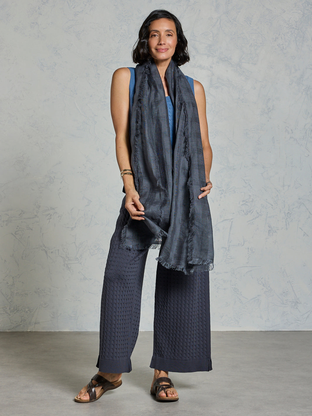 Woman wearing a dark gray scarf and pants against a plain background